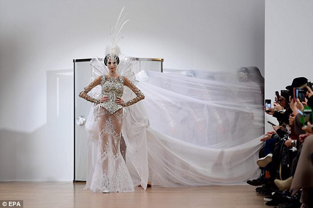 Một thiết kế váy cưới ấn tượng hàng đầu trong buổi trình diễn với phần voan dài được nâng đỡ bởi những người mẫu đứng ở bên trong dải voan.